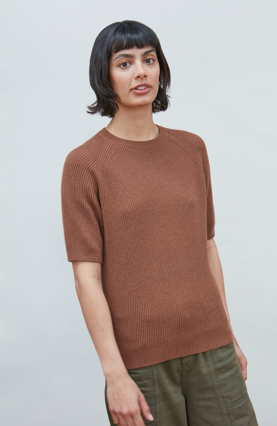 A womens rust ribbed knit short-sleeve sweater with a crew neck by paul james knitwear, displayed flat against a light gray background.