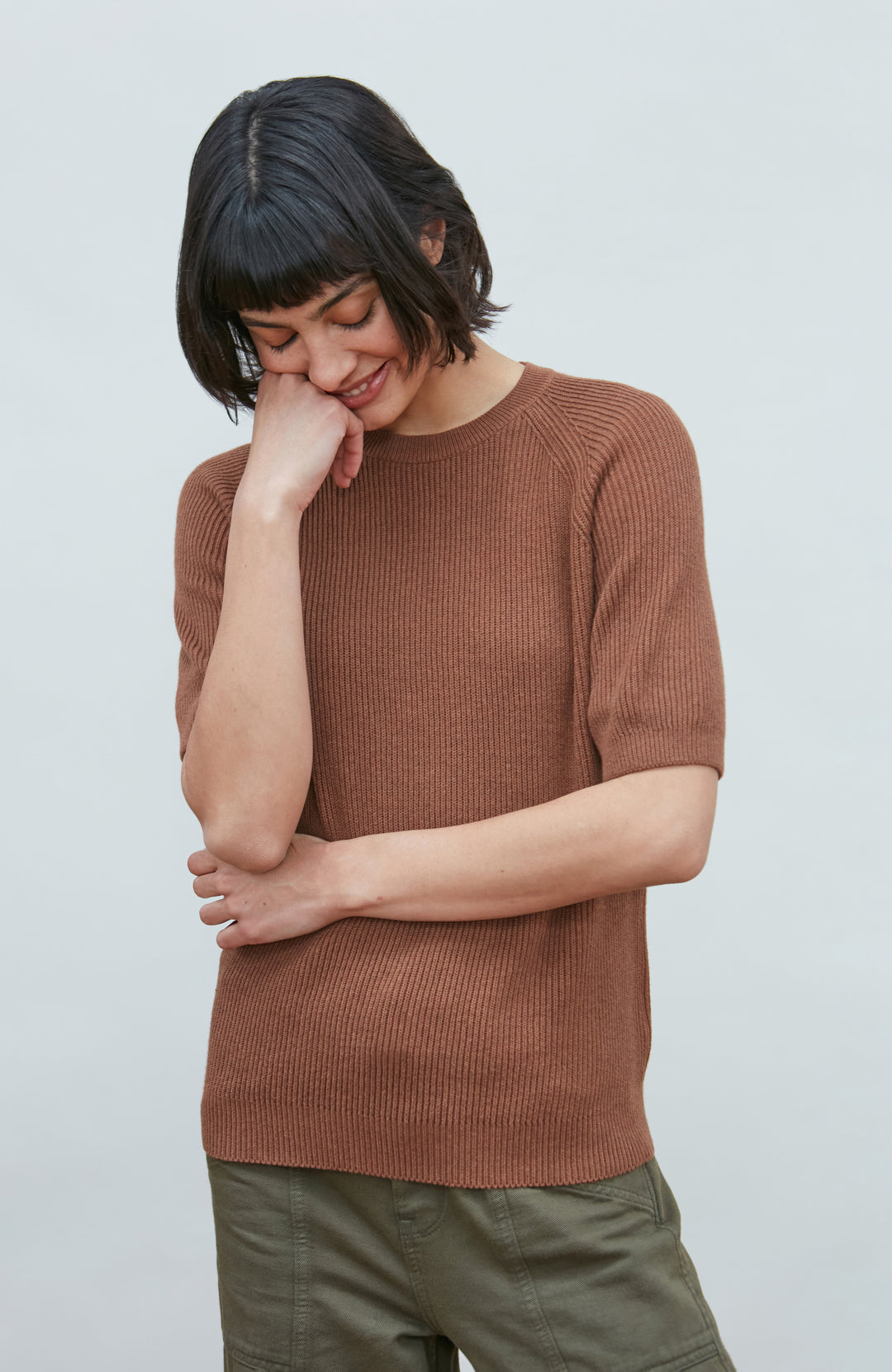 A woman wearing a dark navy blue ribbed short-sleeve mock neck top by paul james knitwear and dark blue jeans, posing against a light gray background.