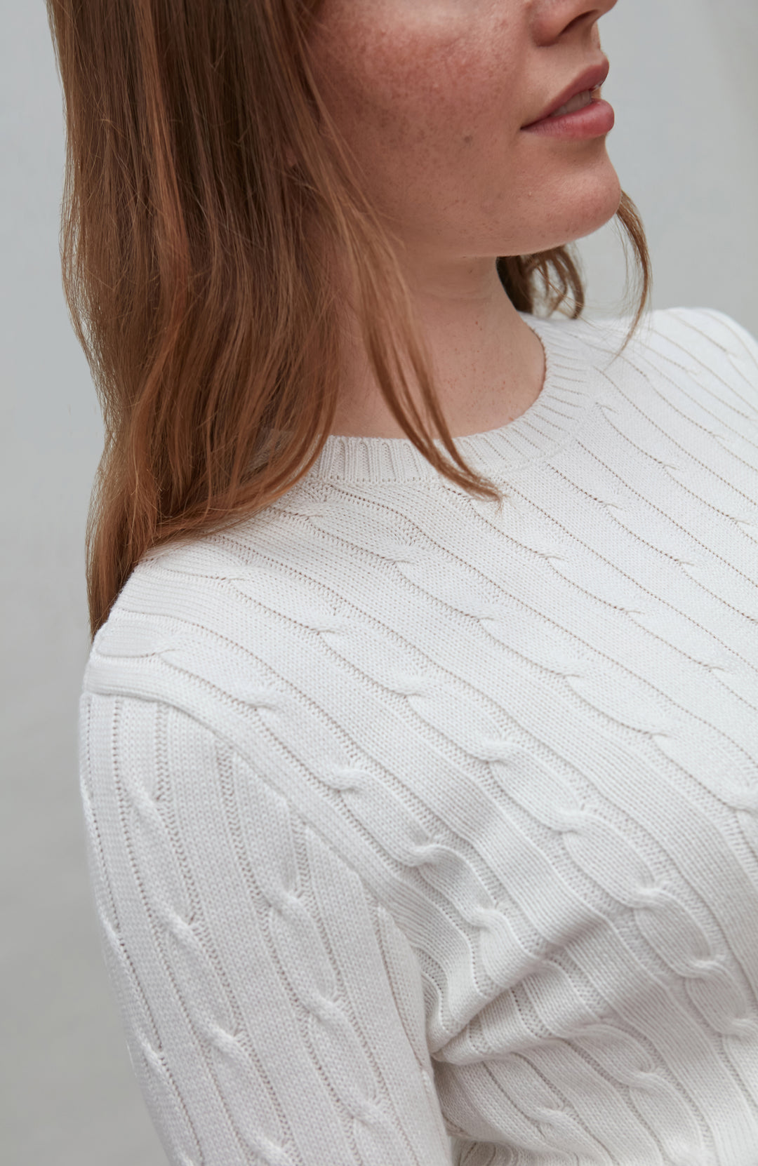 Close-up of a person wearing a white cable knit sweater against a neutral background