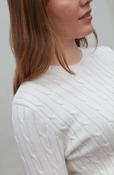 Close-up of a person wearing a white cable knit sweater against a neutral background