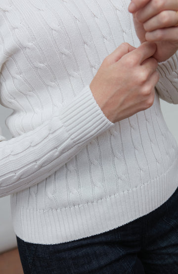 Close-up of a person wearing a white cable knit sweater with a blurred background