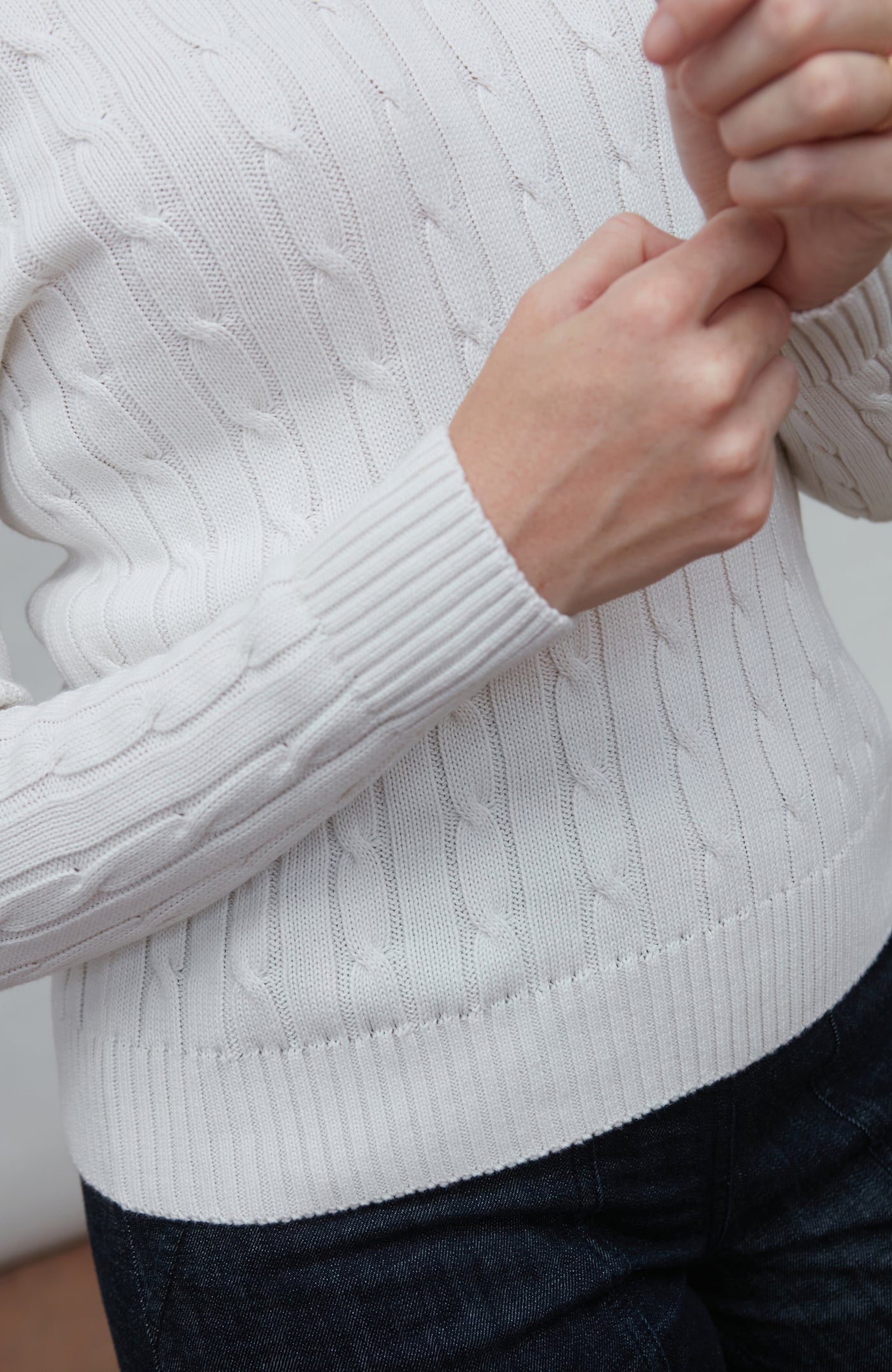 Close-up of a person wearing a white cable knit sweater with a blurred background