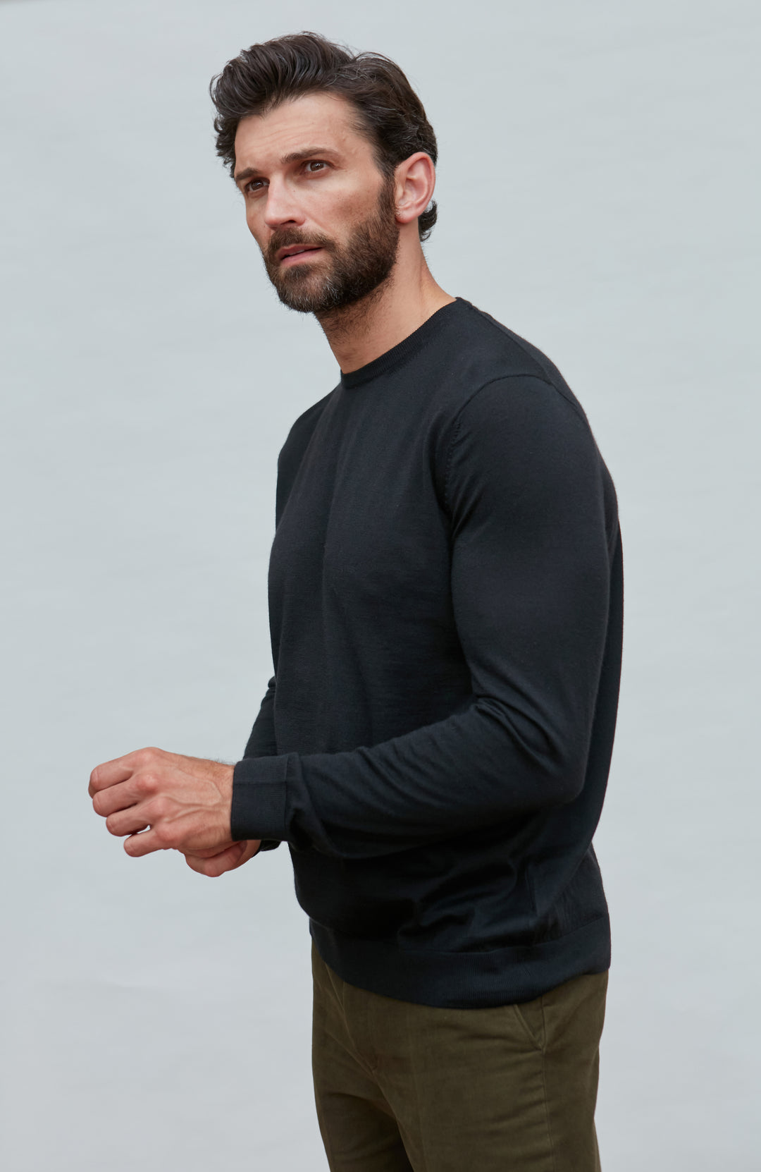 Man wearing a black merino silk sweater  against a light gray background