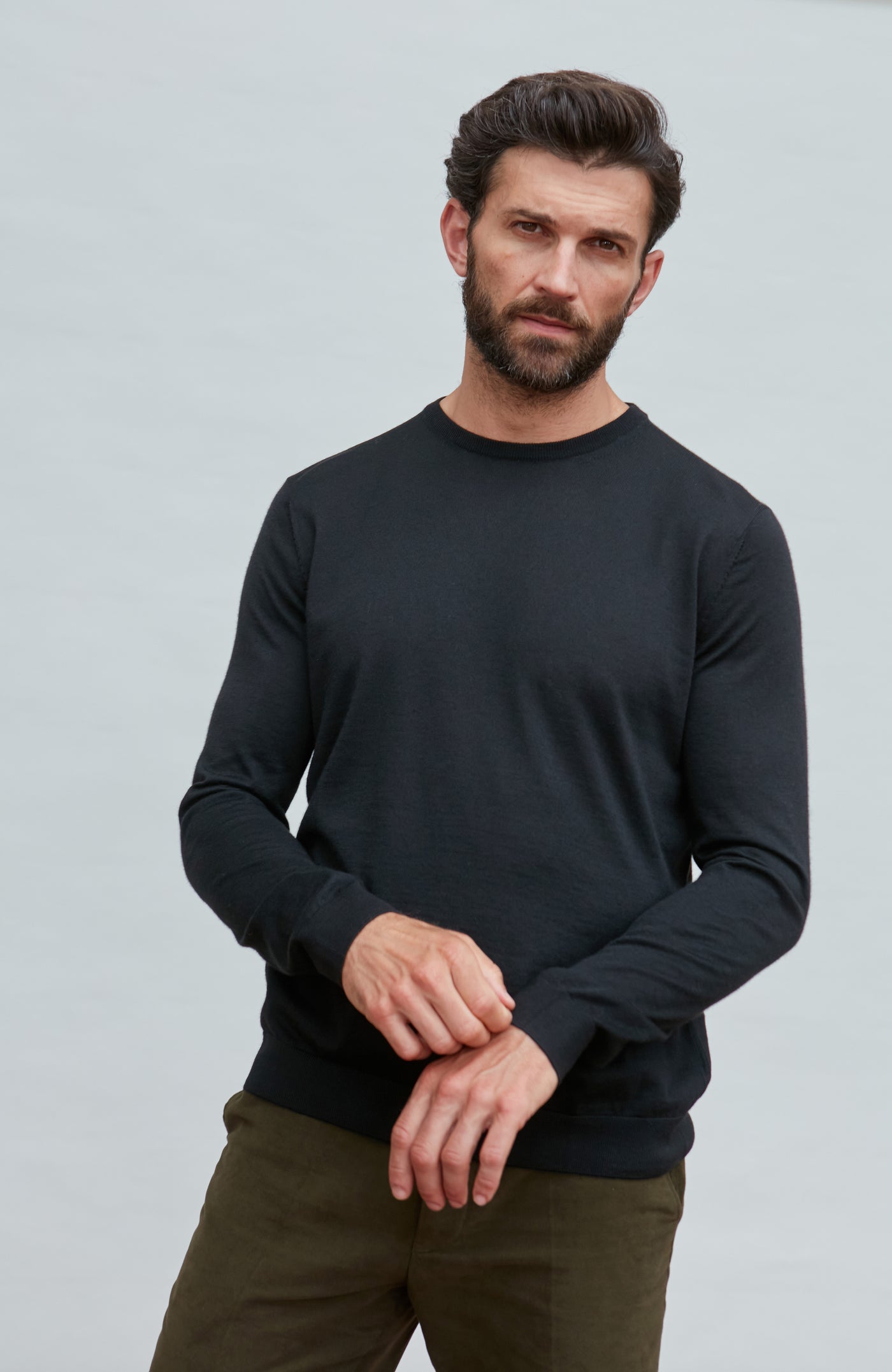 Man wearing a black merino silk sweater  long-sleeve shirt against a gray background