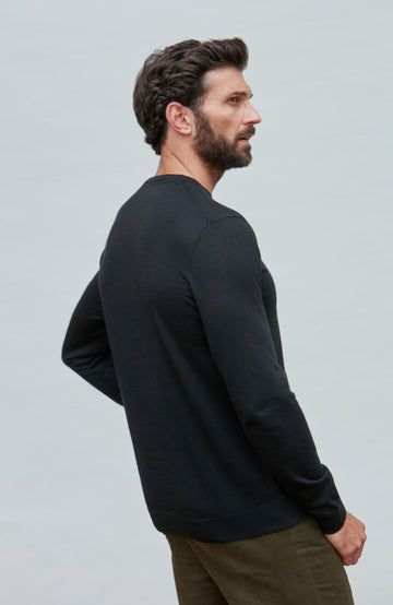 Man wearing a black merino silk sweater  against a light gray background