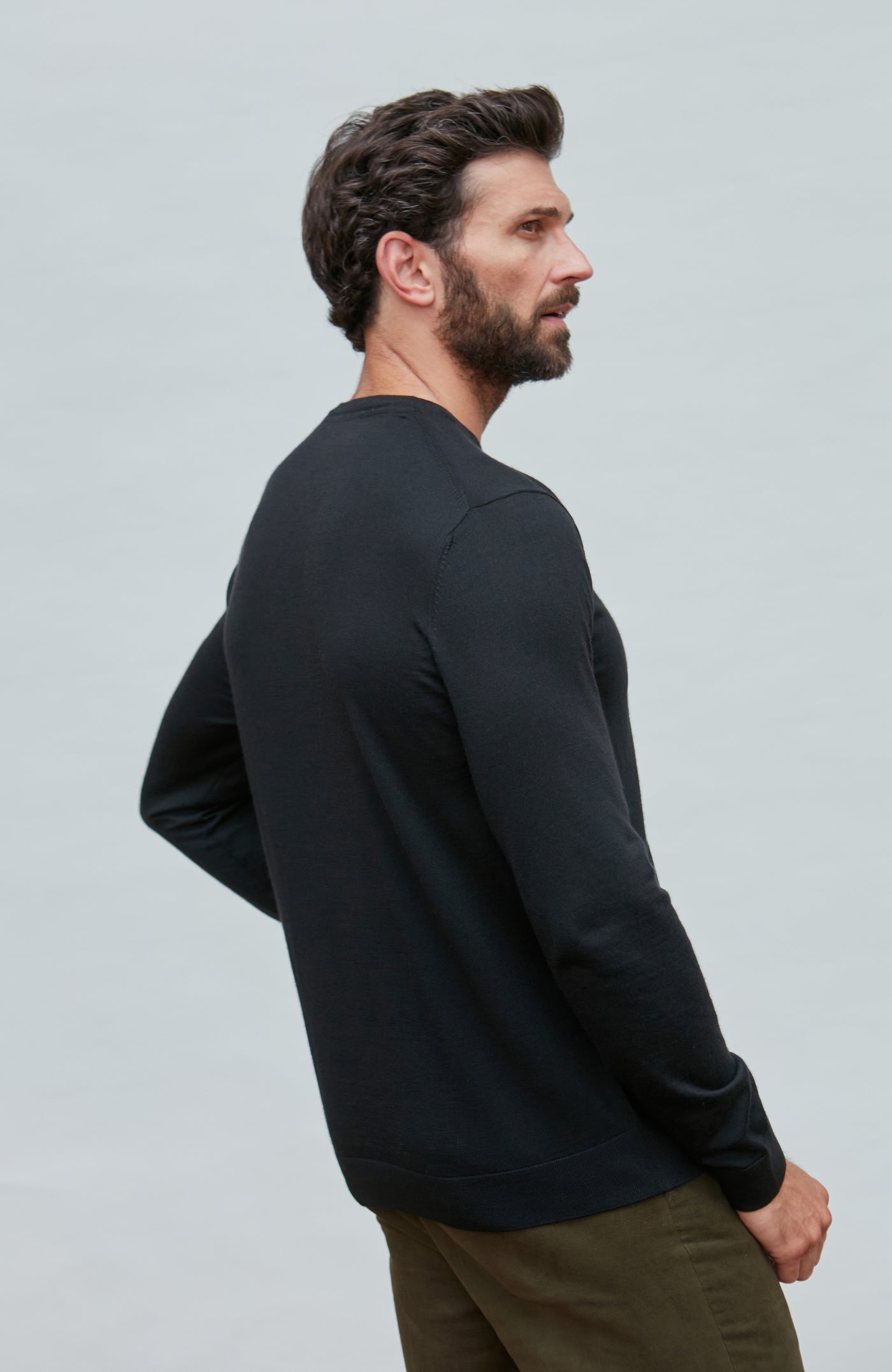 Man wearing a black merino silk sweater  against a light gray background