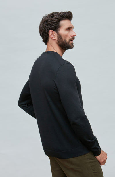 Man wearing a black merino silk sweater  against a light gray background