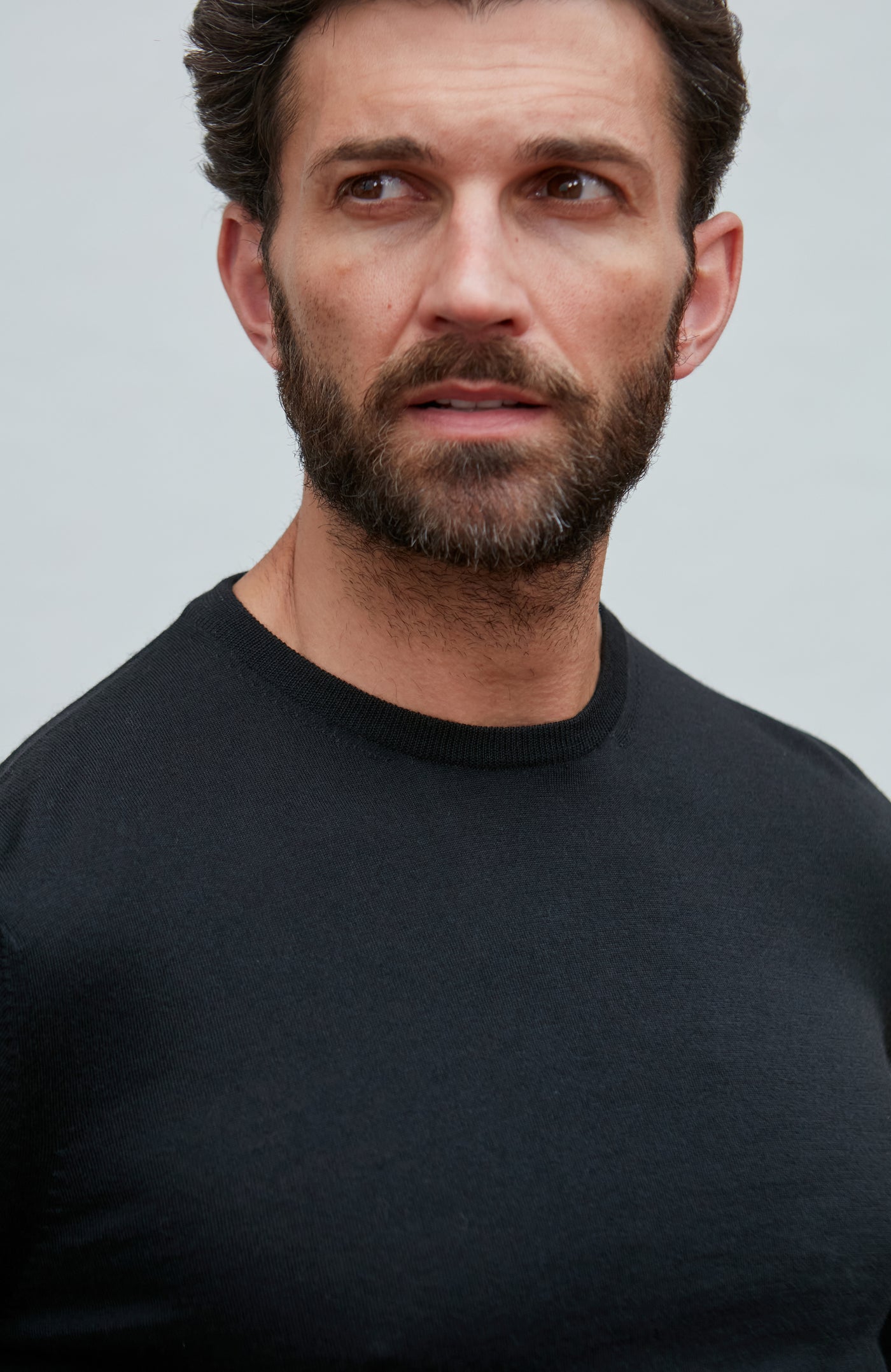 Man wearing a black merino silk sweater  against a light gray background
