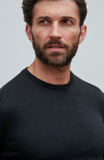 Man wearing a black merino silk sweater  against a light gray background