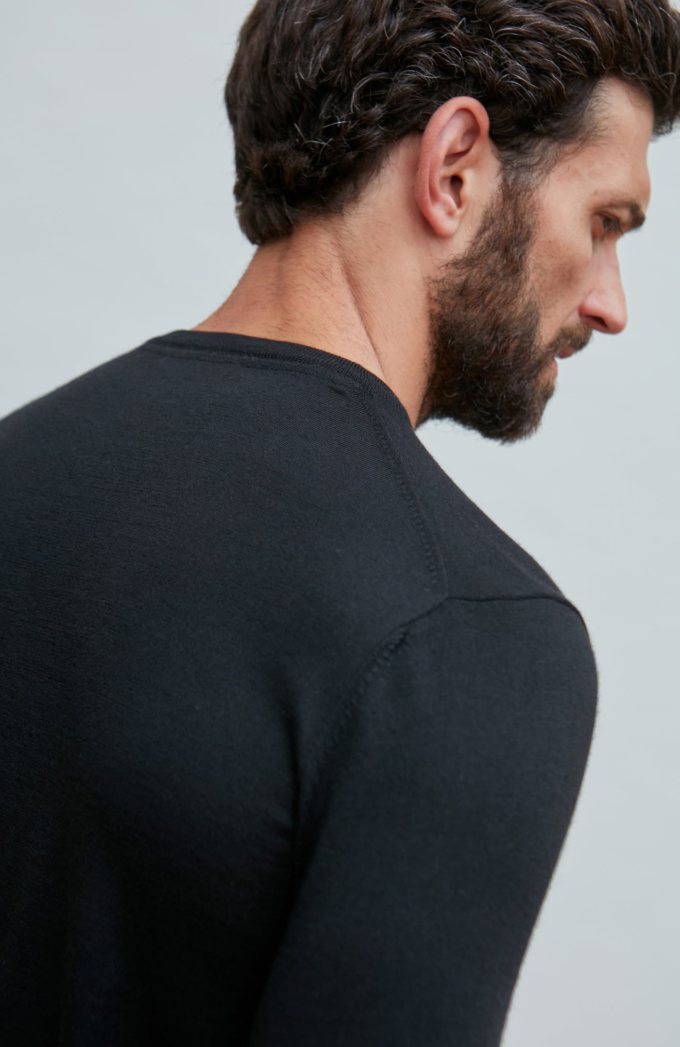 Man wearing a black merino silk sweater  against a light gray background