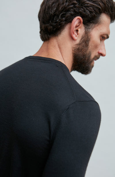 Man wearing a black merino silk sweater  against a light gray background