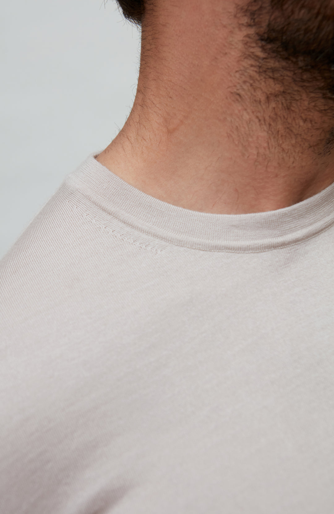 Close-up of a person wearing abeige fine wool silk luxury t-shirt by Paul James against a plain background