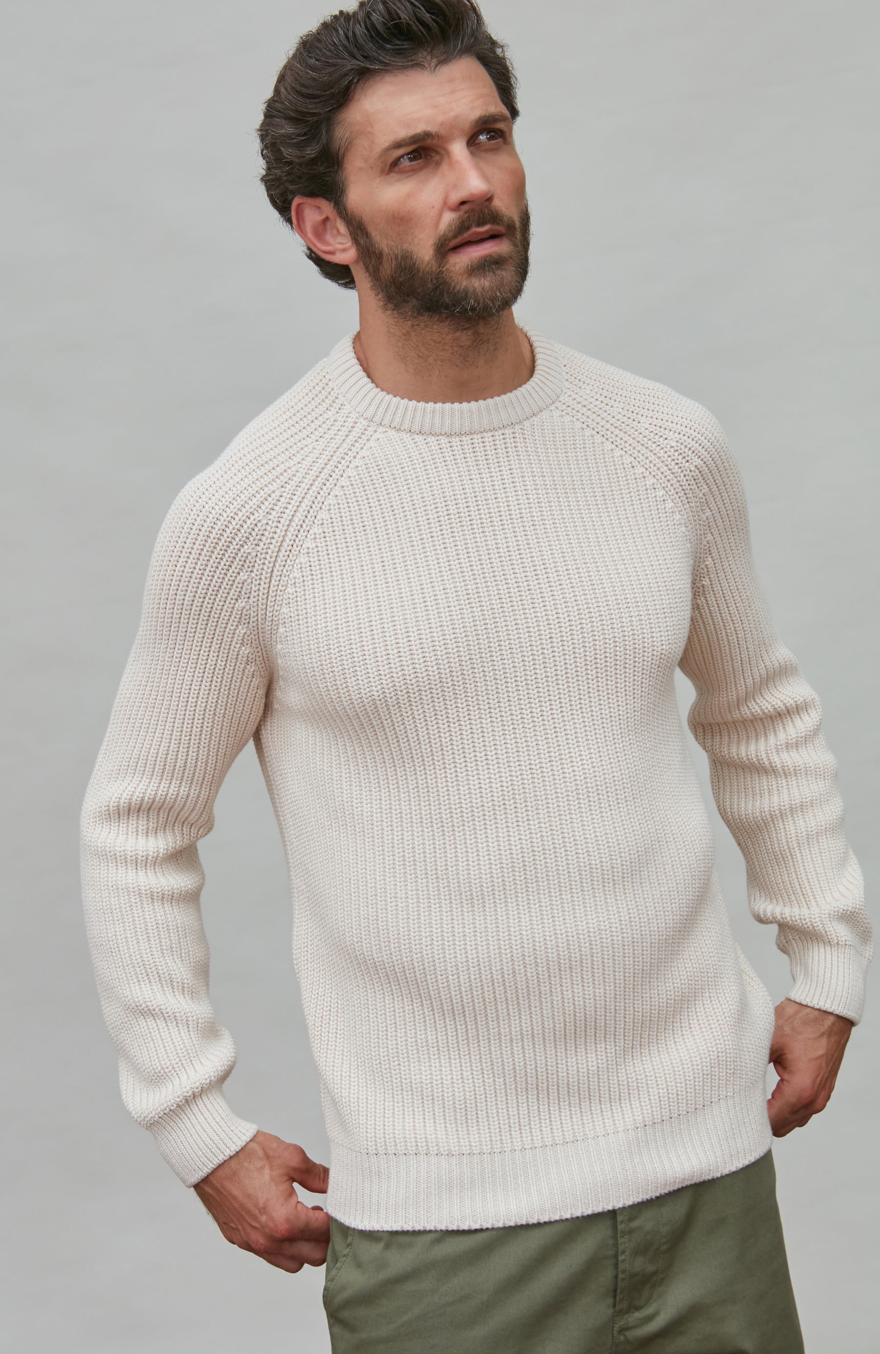 Man wearing a cream cotton rib sweater against a gray background