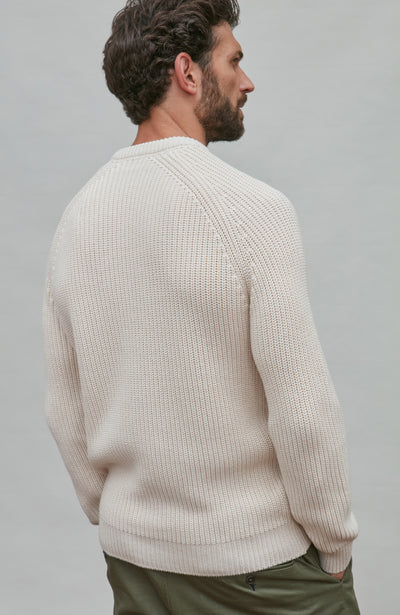 Man wearing a ecru fisherman rib sweater against a plain background