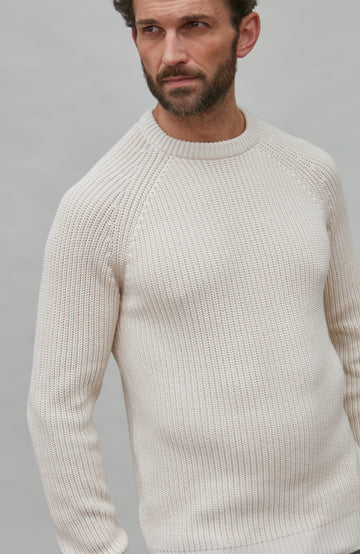 Man wearing a white rib sweater against a gray background