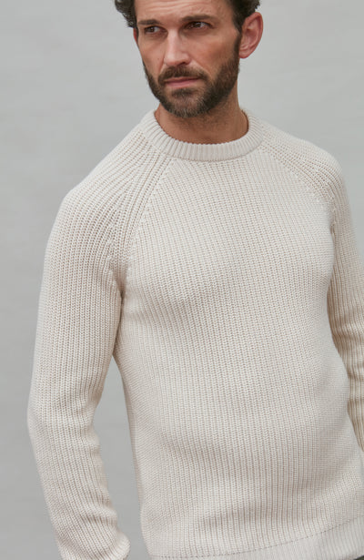 Man wearing a white rib sweater against a gray background