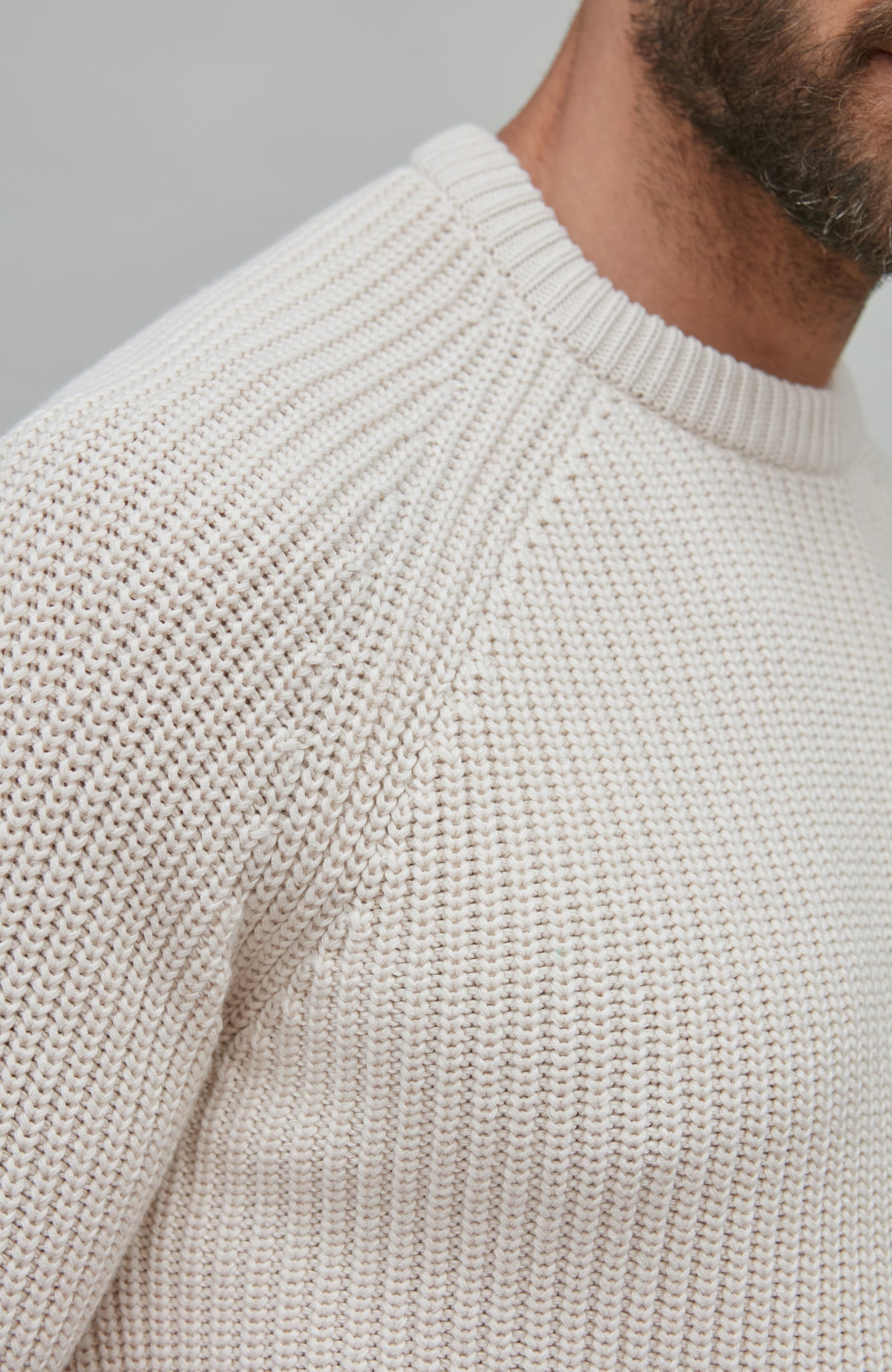 Close-up of a ecru fisherman rib knit sweater on a neutral background
