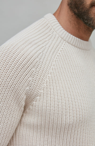 Close-up of a ecru fisherman rib knit sweater on a neutral background
