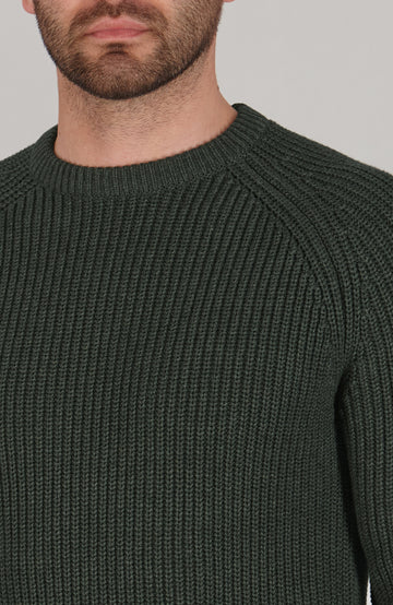 Close-up of a person wearing a dark green ribbed sweater against a neutral background
