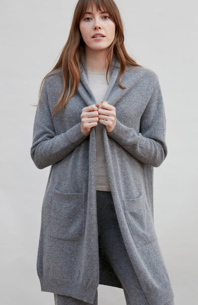 Woman wearing a long wool gray cardigan against a plain background