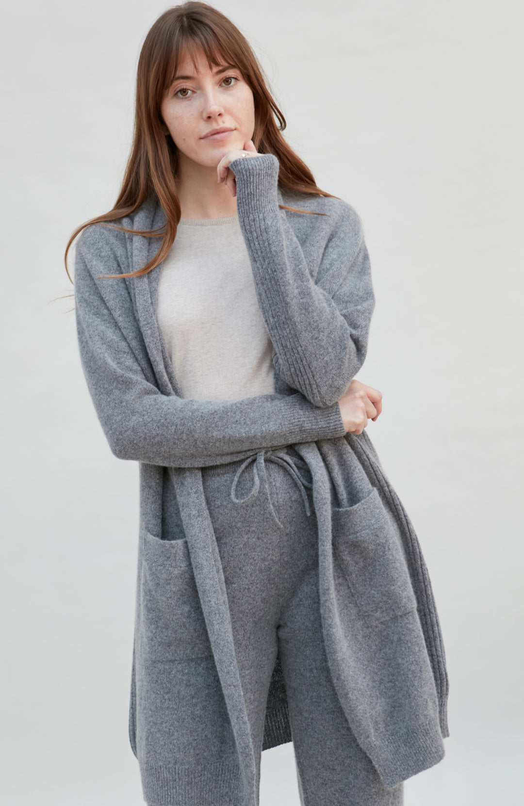 Woman wearing a gray wool cardigan over a white top on a plain background