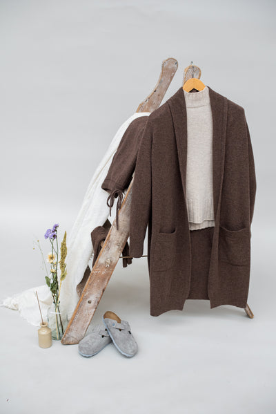 Brown wool cardigan, white shirt, gray slippers, and wooden shoes on a white background