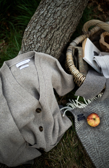Gray WOOL CARDIGAN with buttons on a grassy ground next to a tree by Paul James