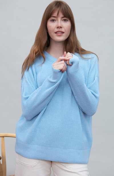 Woman wearing a light blue cotton fisherman rib sweater against a plain background