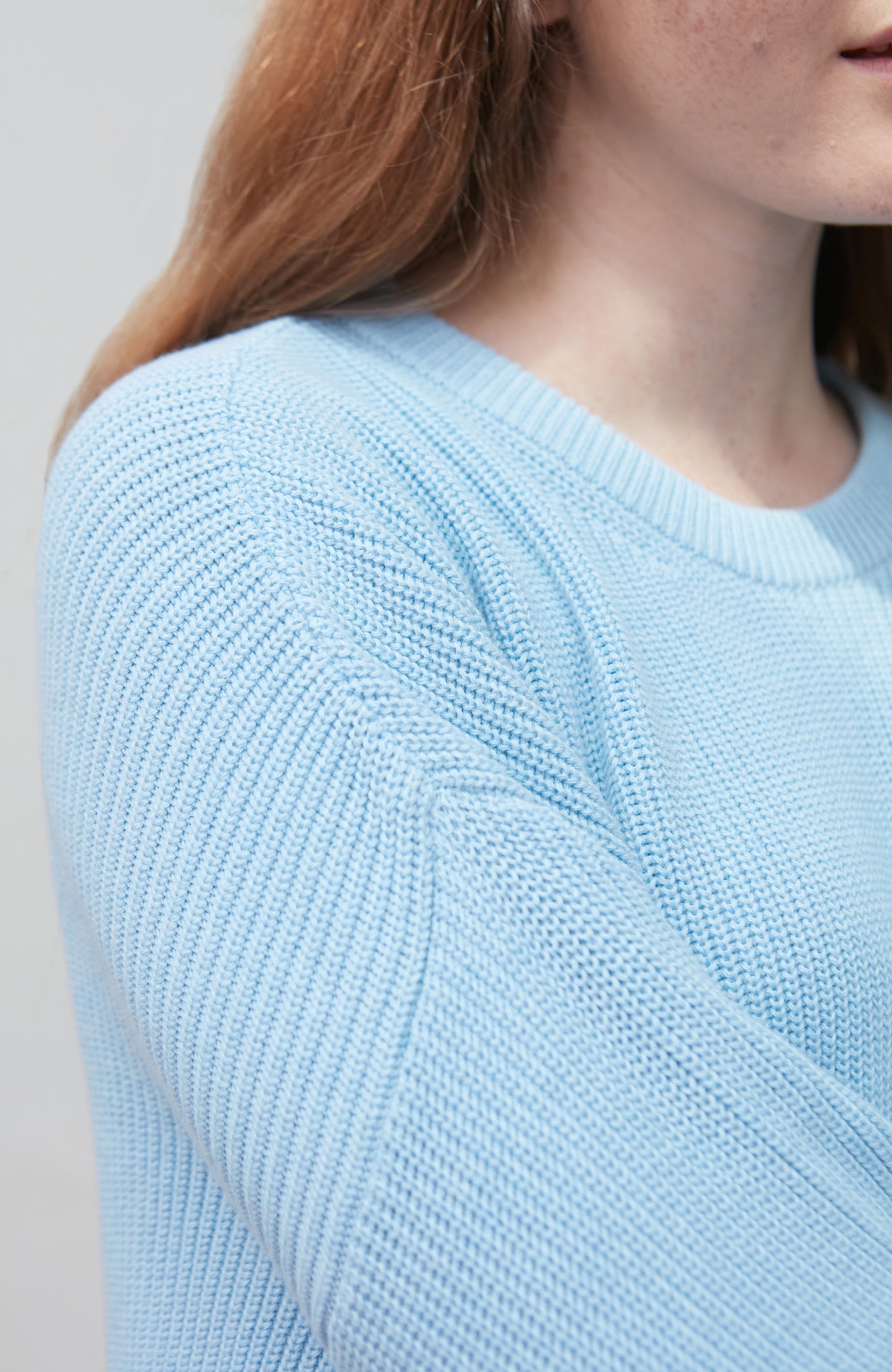 Light blue cotton fisherman rib knitted sweater worn by a person with a neutral background