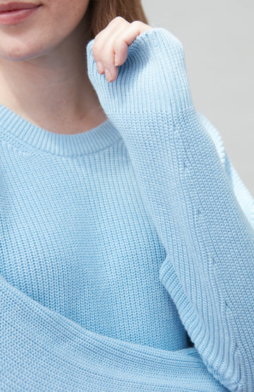 Light blue knitted cotton fisherman rib sweater worn by a person, with a neutral background