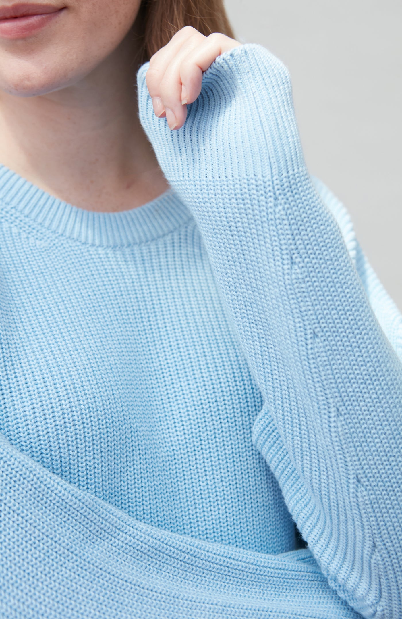 Light blue knitted cotton fisherman rib sweater worn by a person, with a neutral background