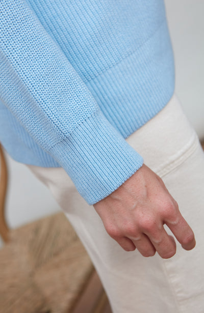 Light blue cotton fisherman rib sweater sleeve and white pants with a blurred background