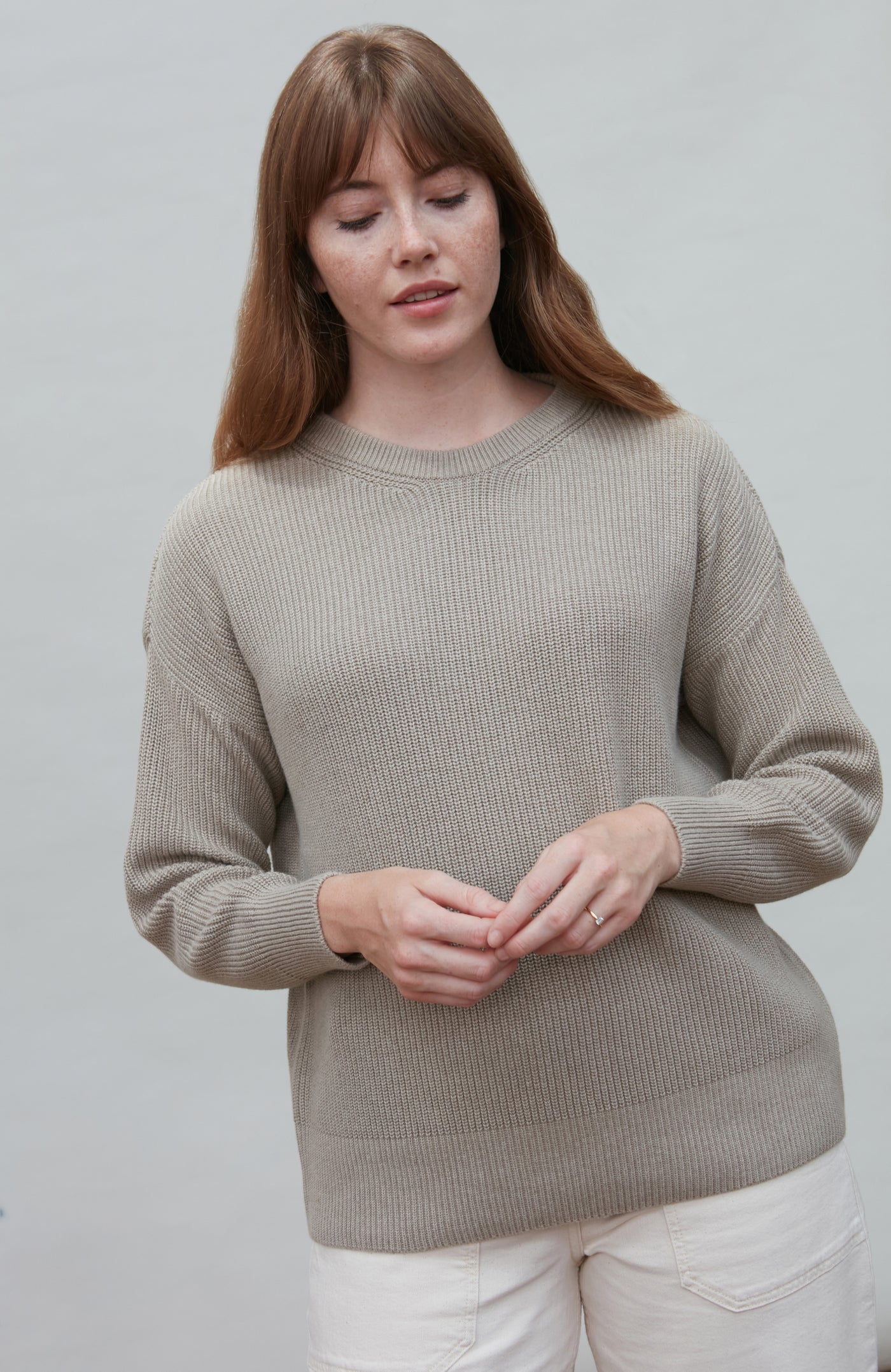 Woman wearing a beige cotton fisherman rib sweater against a plain background