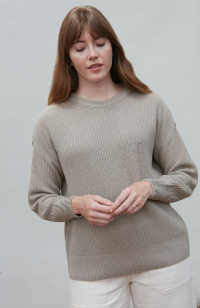 Woman wearing a beige cotton fisherman rib sweater against a plain background