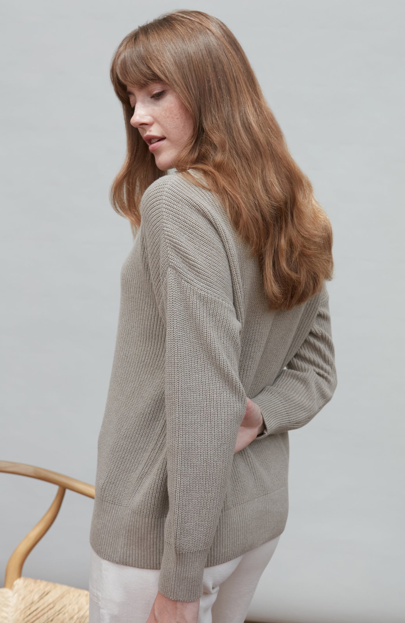 Woman wearing a cotton fisherman rib sweater against a plain background