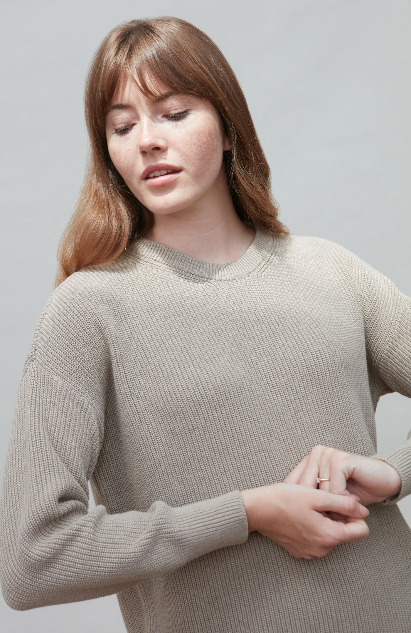 Woman wearing a beige cotton fisherman rib sweater against a plain background