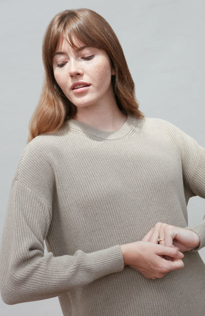 Woman wearing a beige cotton fisherman rib sweater against a plain background