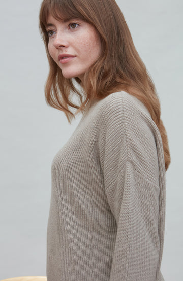 Woman wearing a beige cotton fisherman rib sweater against a plain background
