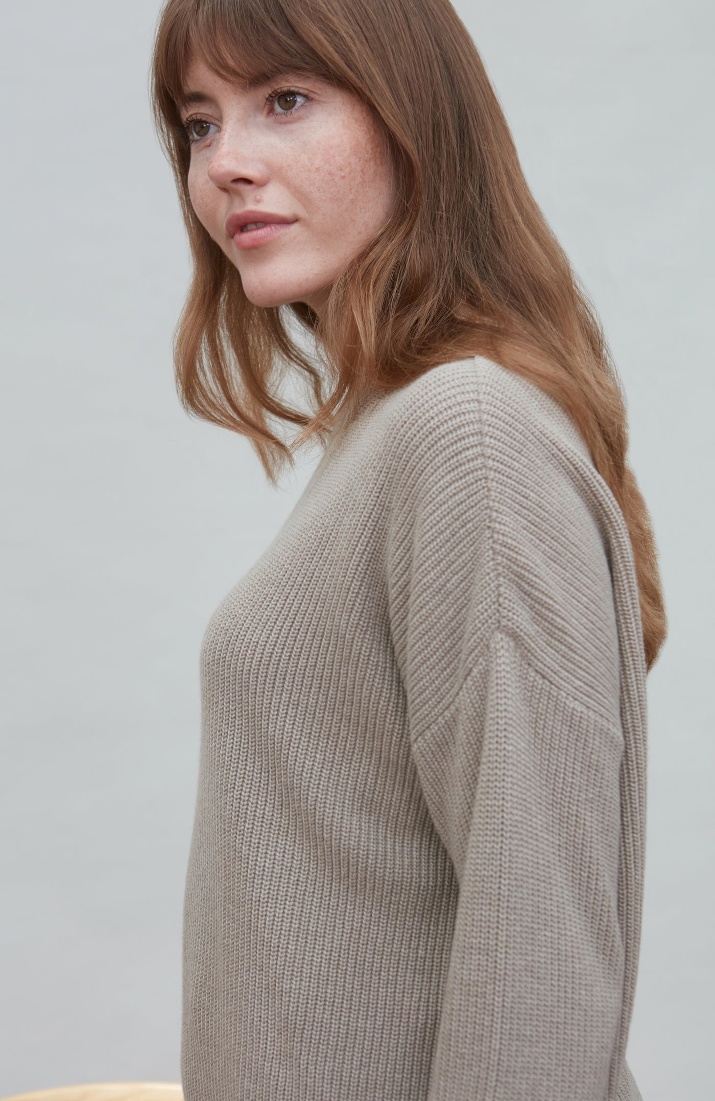 Woman wearing a beige cotton fisherman rib sweater against a plain background