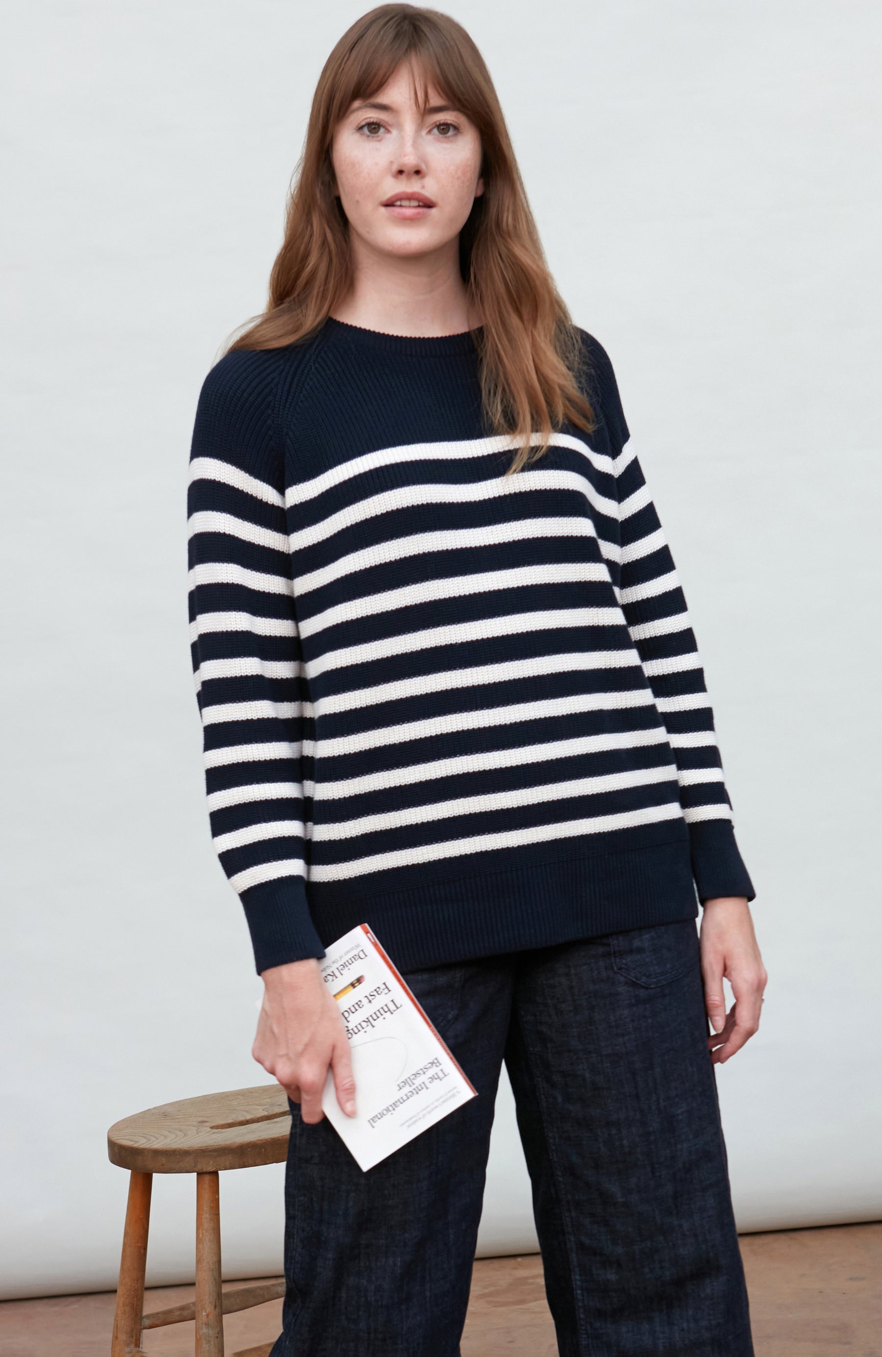 Woman wearing a navy and white striped ribbed crew sweater holding a piece of paper.