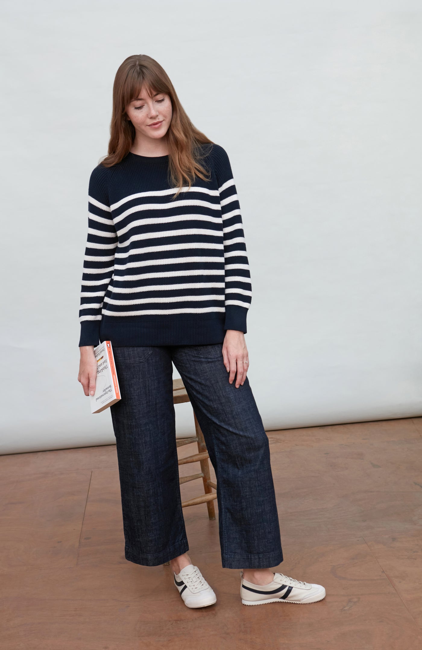 Woman wearing a navy and white striped rib breton sweater with dark jeans, standing against a plain background.