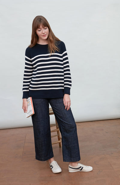 Woman wearing a navy and white striped rib breton sweater with dark jeans, standing against a plain background.