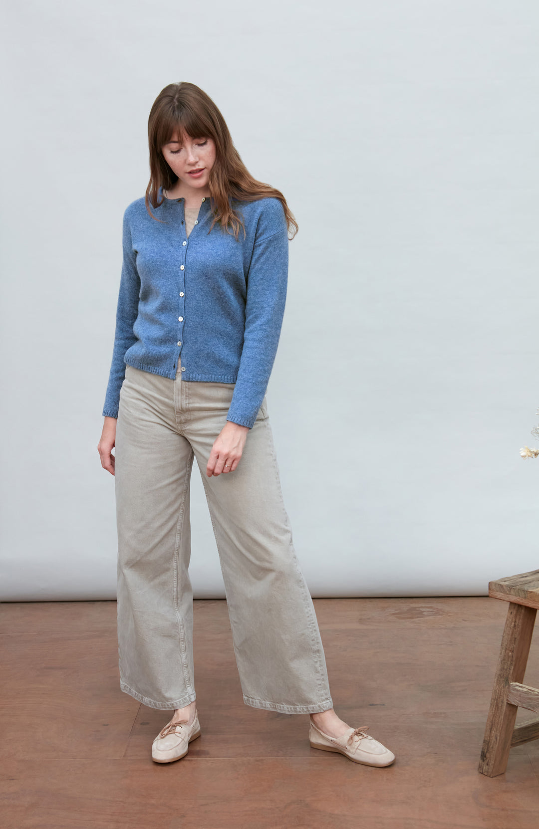 Woman wearing a blue wool cardigan and beige pants standing against a plain background by Paul James