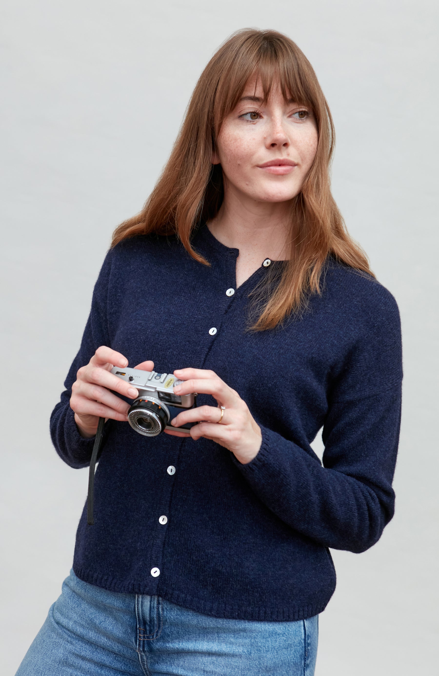 Woman wearing a navy blue wool cardigan holding a camera against a plain background