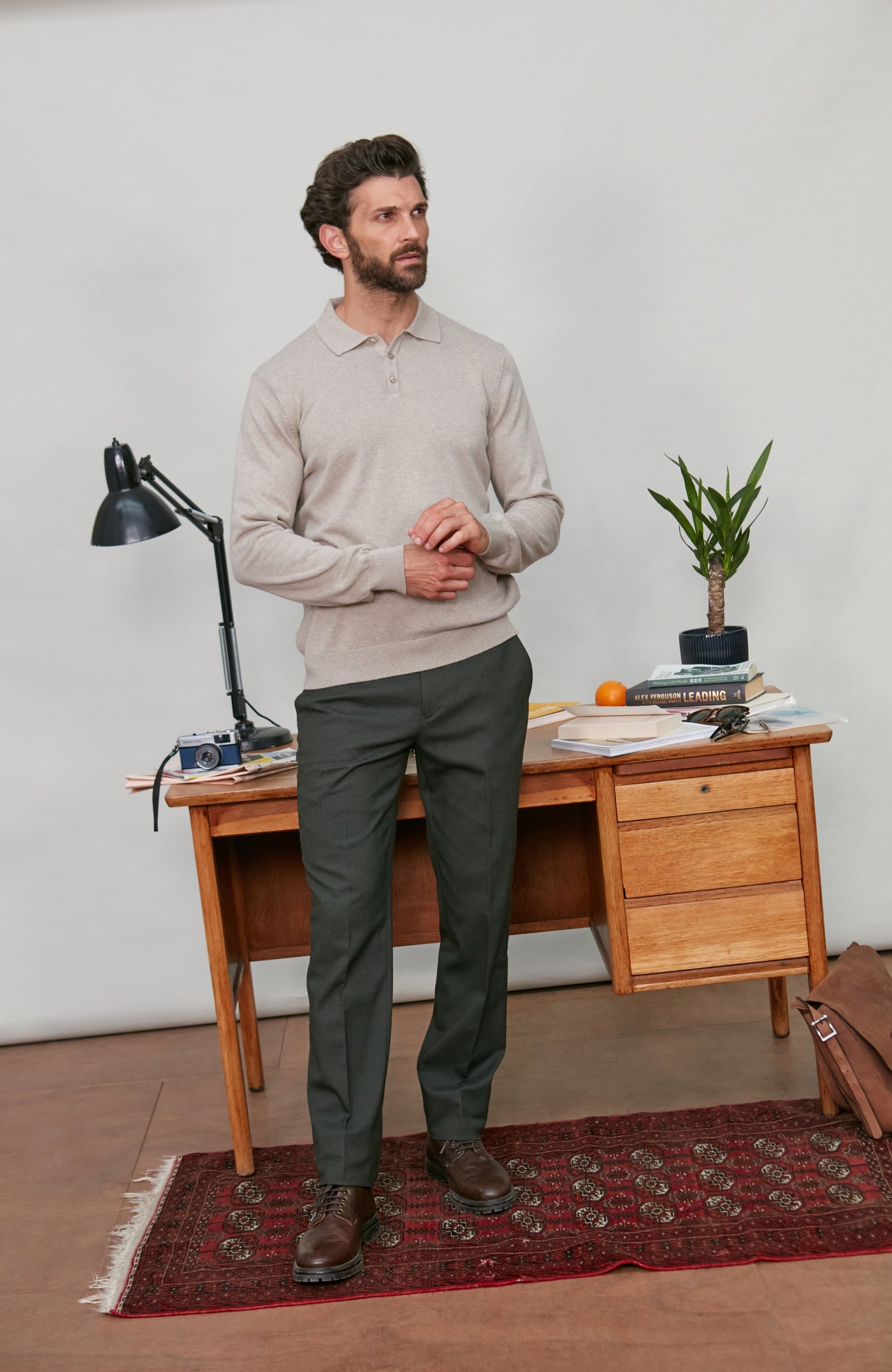 Man polo neck sweater standing in a room with a wooden desk and lamp