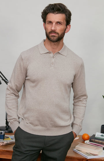 Man wearing a beige polo neck sweater standing in a room with a desk and books.