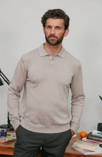 Man wearing a beige polo neck sweater standing in a room with a desk and books.