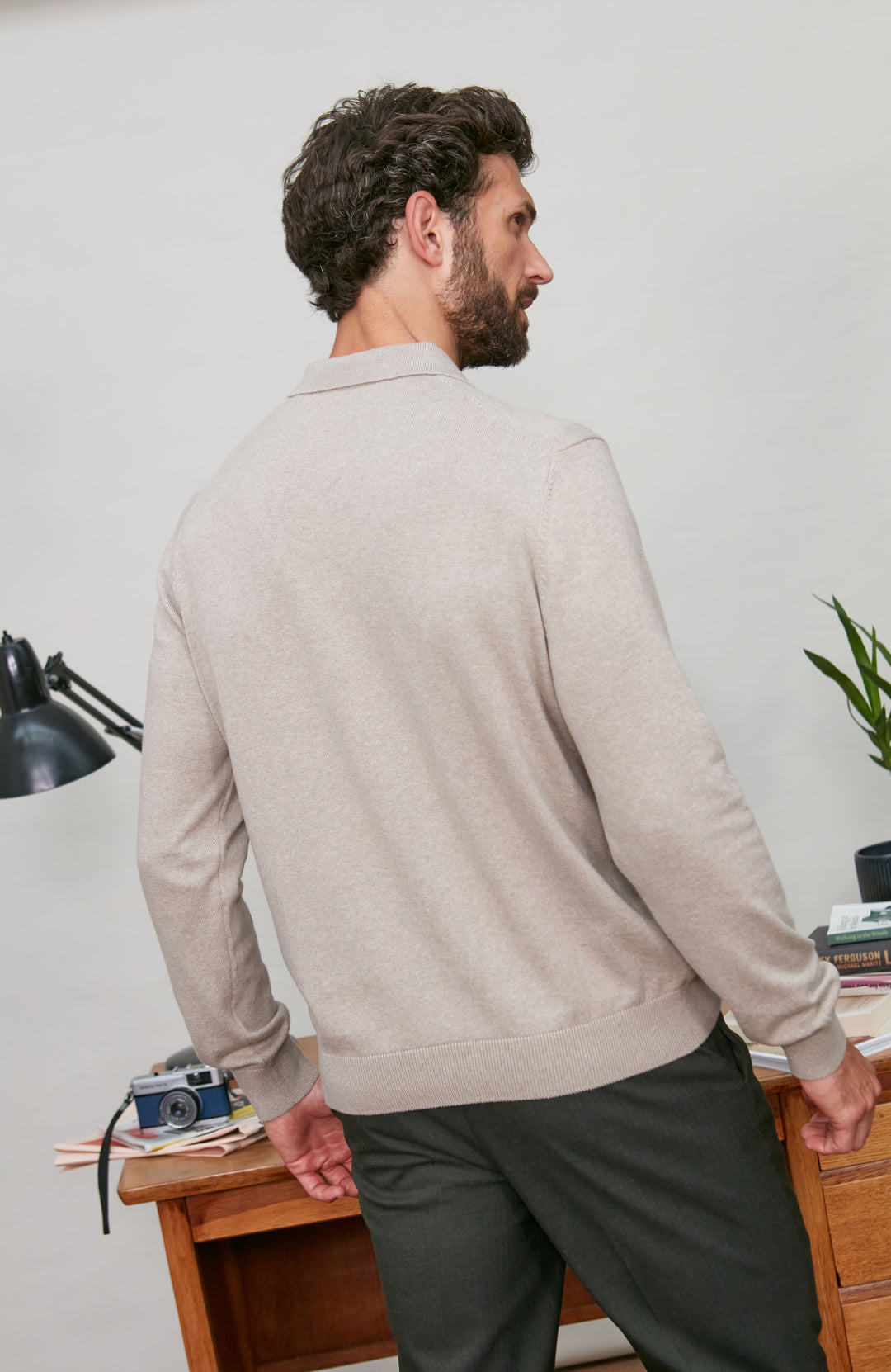 Man wearing a beige sweater and dark pants in an indoor setting.