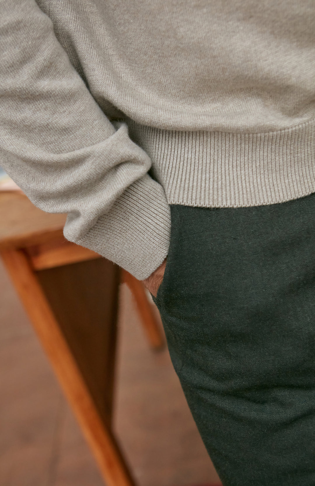 Person wearing a beige sweater and dark pants sitting on a wooden bench.