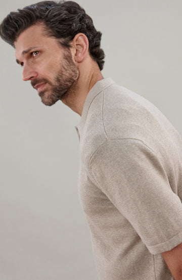 A man wearing a light beige short-sleeve cotton knit button-up shirt by paul james knitwear